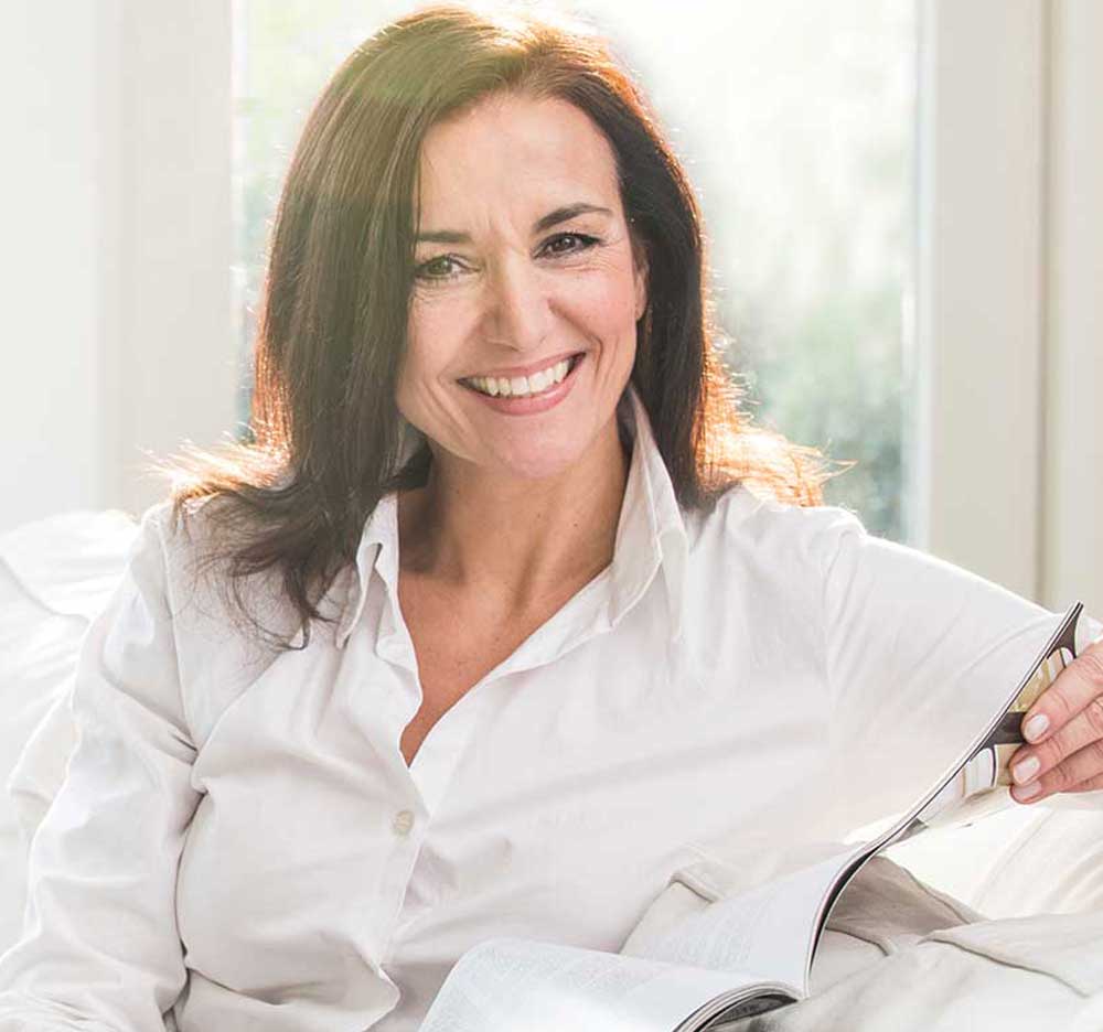 Middle aged woman with a bright smile reading a magazine.